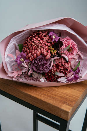 Bouquet of flowers in pink package on wooden chair on a light background. Rosa, carnation, chrysanthemum, cotinus, pistach, brunia, clematis.の写真素材