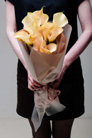 Bouquet of calla flowers in beige package in the hands of a woman florist.の写真素材