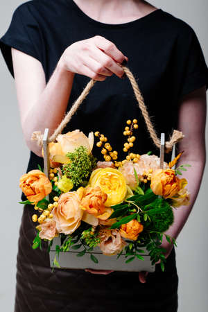 Bouquet of flowers in a wooden box in the hands of a woman florist. Rosa spray Catalina, ilex, skimmia, carnation, eustoma, tulipの写真素材
