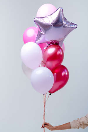 Composition of red, pink, transparent helium balloons and silver star in the hand of a woman on a white background.の写真素材