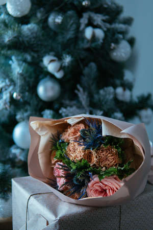 Bouquet of flowers in peach package on gift box wrapped in craft paper on the background of Christmas tree. Rosa, carnation, eryngium, eucalyptus.の写真素材