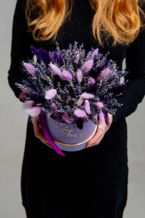 Bouquet in lilac hat box of dried flowers in the hands of red-haired girl florist on light background. Lagurus, hydrangea.の写真素材