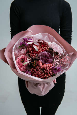 Bouquet of flowers in pink package in the hands of a woman florist on a light background. Rosa, carnation, chrysanthemum, cotinus, pistach, brunia, clematis.の写真素材
