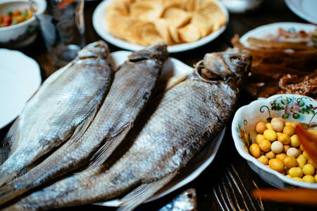salted fish, chips, peanuts, snacks on white plates on a wooden tableの写真素材