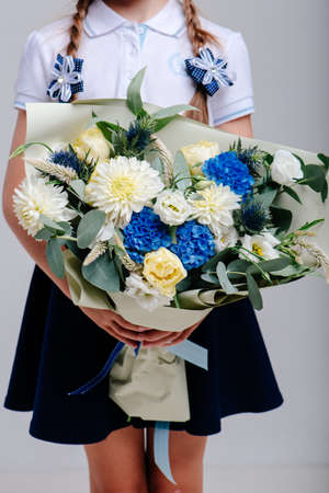A bouquet of flowers, packed in beige paper in the hands of a girl with pigtails on a light background. Bouquet of hydrangea, dahlia, tulip, eustoma, celosis, eucalyptusの写真素材