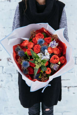 Bouquet of flowers in pink transparent package in hands of woman florist in knitted sweater on background white brick wall.の写真素材