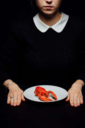 girl boiled crayfish in the hands on a white plate on a black backgroundの写真素材