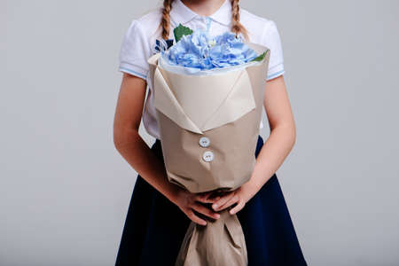 A bouquet of hydrangea, packed in beige paper in the hands of a girl with pigtails on a light background.の写真素材