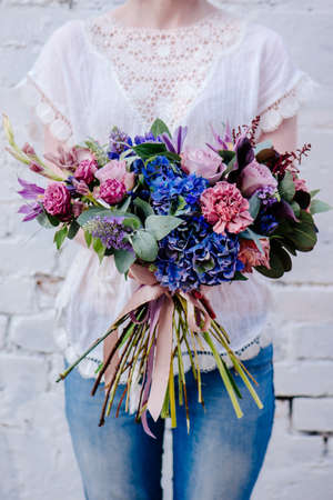 A bouquet of flowers in the hands of a woman on a light background. Bouquet of Eucalyptus, Carnation, Hydrangea, Rose, Clematis, Cotinusの写真素材