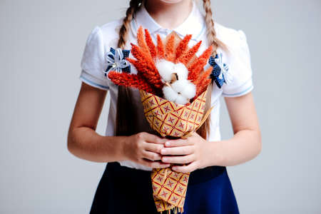 A small bouquet of Amaranthus and cotton bolls, packed in craft paper in the hands of a girl with pigtails on a light backgroundの写真素材