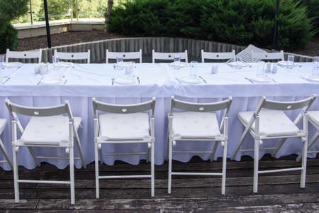 White served table with many chairs outdoor on background of green treesの写真素材