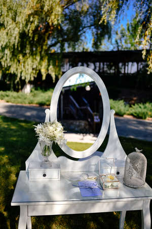 Place for a photo for the bride. White luxury chair stands before a mirror and wedding flower arrangements on the green lawn outsideの写真素材