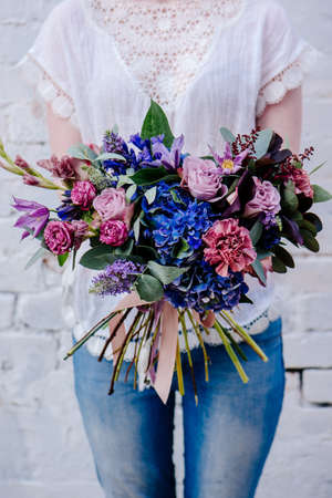 A bouquet of flowers in the hands of a woman on a light background. Bouquet of Eucalyptus, Carnation, Hydrangea, Rose, Clematis, Cotinusの写真素材