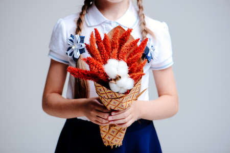 A small bouquet of Amaranthus and cotton bolls, packed in craft paper in the hands of a girl with pigtails on a light backgroundの写真素材