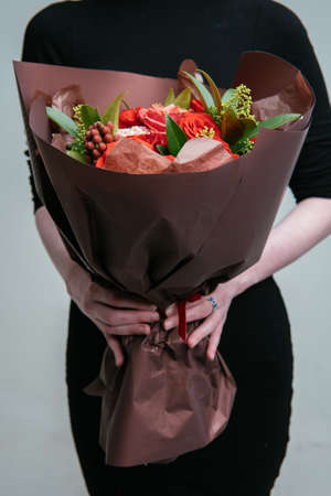 Bouquet of flowers in burgundy package in the hands of a woman florist on light background. Rosa, skimmy, carnation, brunia.の写真素材