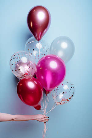 Composition of white, pink, transparent helium balloons in the hand of a woman on a blue background.の写真素材