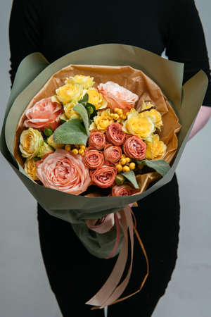 Bouquet of flowers in pistachio-colored package in the hands of a woman florist on light background. Rosa, stahis, ilexの写真素材