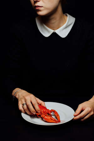 girl boiled crayfish in the hands on a white plate on a black backgroundの写真素材