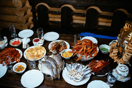 boiled crayfish, salted fish, smoked fish, chips, peanuts, snacks on white plates on a wooden tableの写真素材
