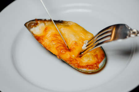 baked mussel in a shell with cheese on a white plate with a knife and forkの写真素材