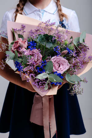 A bouquet of flowers, packed in purple paper in the hands of a girl with pigtails on a light background. Bouquet of Rose, Eucalyptus, Carnation, Limonium, Brassicaの写真素材