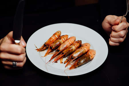 fried shrimp on a white plate knife and fork in hand on a black backgroundの写真素材