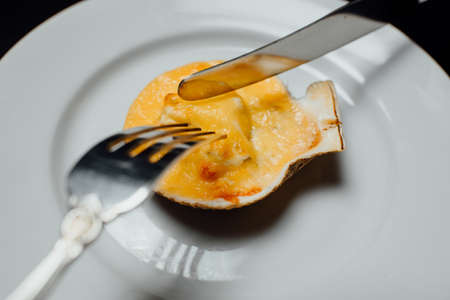 baked scallops in a shell with cheese on a white plate with a knife and fork on a black background