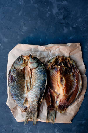Three crucian carp smoked fish on craft paper on dark backgroundの写真素材