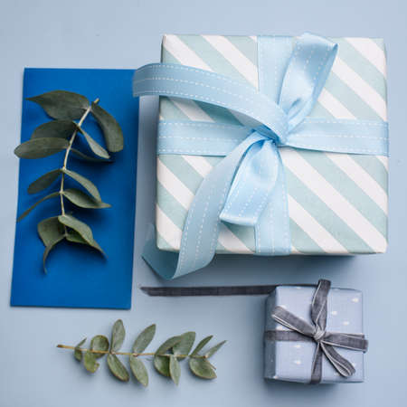 Two blue gift boxes, a blue gift envelope with eucalyptus twigs on a blue backgroundの写真素材