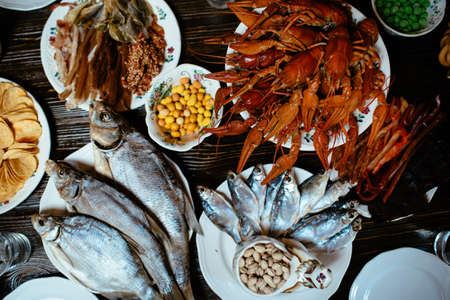 boiled crayfish, salted fish, smoked fish, chips, peanuts, snacks on white plates on a wooden tableの写真素材