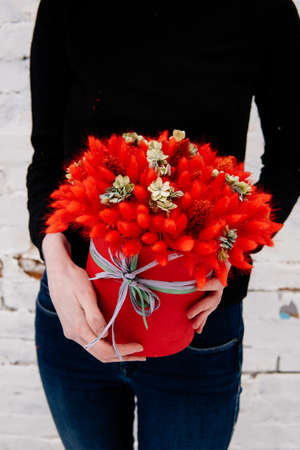 Bouquet in red hat box of dried flowers in the hands of a woman florist on background a white brick wall. Lagurus, hydrangea.の写真素材