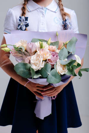 A bouquet of flowers, packed in purple paper in the hands of a girl with pigtails on a light background. Bouquet of Rose, Eucalyptus, Eustoma, Stipaの写真素材