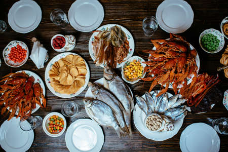 boiled crayfish, salted fish, smoked fish, chips, peanuts, snacks on white plates on a wooden tableの写真素材