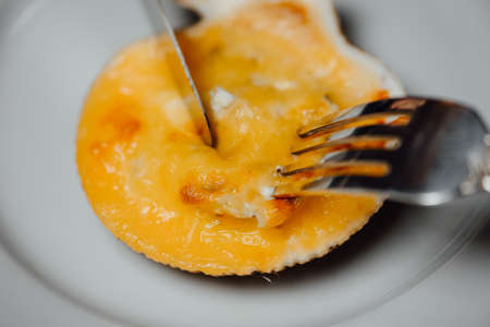 baked scallops in a shell with cheese on a white plate with a knife and fork on a black background