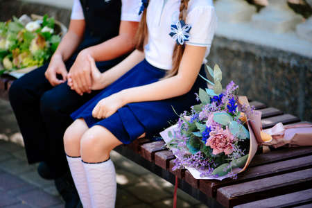 Girl and boy are sitting on a bench and holding hands. On the bench is a bouquet of flowers in purple packaging. Bouquet of Rose, Eucalyptus, Carnation, Limonium, Brassicaの写真素材
