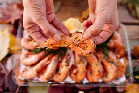 Fried shrimps with lemon and dill in hands of woman on wooden table with autumn leaves, mushrooms and chestnuts.の写真素材