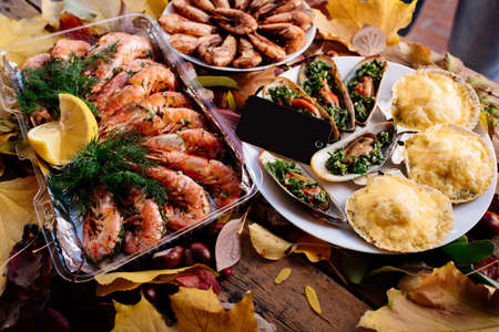 Fried shrimps, baked mussels and scallops baked under cheese on wooden table with autumn leaves and chestnuts for Oktoberfest.の写真素材