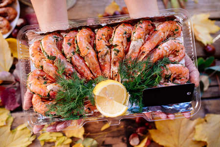 Fried shrimps with lemon and dill in hands of woman on wooden table with autumn leaves, mushrooms and chestnuts for Oktoberfest.の写真素材