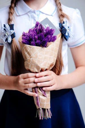 A small bouquet with Phalaris, packed in craft paper in the hands of a girl with pigtails on a light backgroundの写真素材