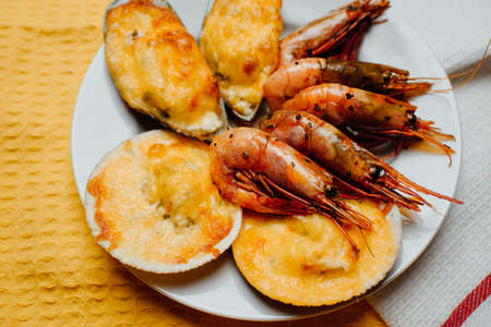 baked scallops and mussels in a shell with cheese, grilled shrimps on a white plate on a yellow backgroundの写真素材