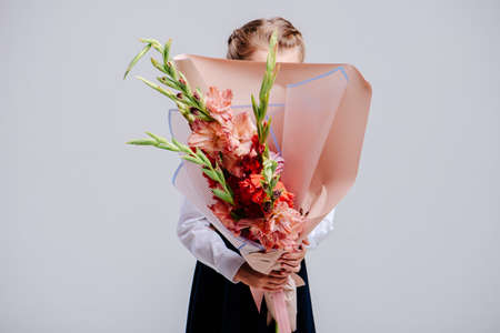 A bouquet of gladiolus, packed in peach paper in the hands of a girl.の写真素材