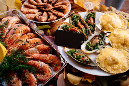 Fried shrimps, baked mussels and scallops baked under cheese on wooden table with autumn leaves and chestnuts.の写真素材