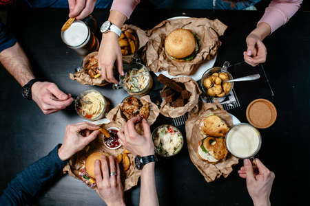 Great menu for beer party with friends. Burger, sandwich, salad, french fries, bread croutons, meat dumplings, fried shrimp, pasta, fried chicken on black tableの写真素材
