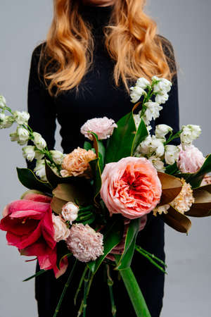 Bouquet of flowers in the hands of red-haired girl florist on light background. Rose, amaryllis, eustoma, delphinium, magnolia leaves.の写真素材