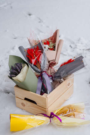 Small beautiful bouquets of dried flowers in various package in wooden box on white snowの写真素材