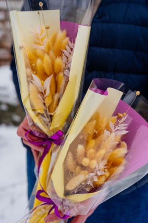 Two small beautiful bouquet of lagurus in transparent and yellow-purple packaging in hands of womanの写真素材