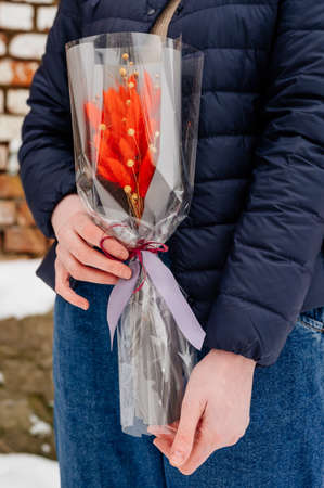Small beautiful bouquet of lagurus in transparent and gray packaging in hands of womanの写真素材
