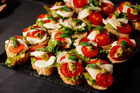 Bruschetta with mozzarella, tomato and pesto sauce on black tableの写真素材