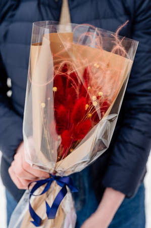 Beautiful bouquet of lagurus in transparent and peach color packaging in hands of womanの写真素材