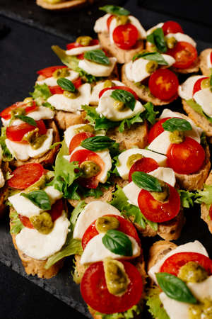 Bruschetta with mozzarella, tomato and pesto sauce on black tableの写真素材
